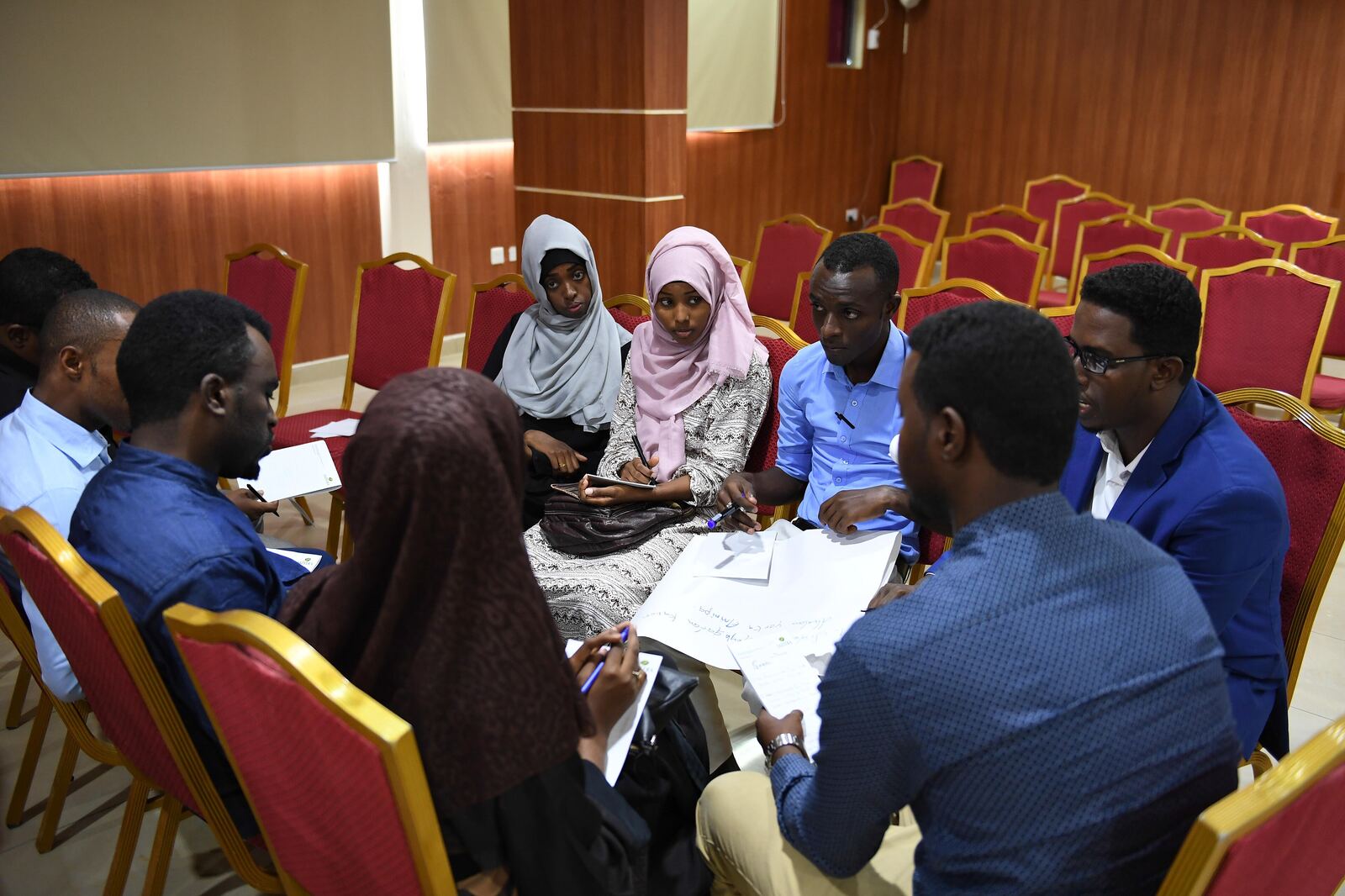 A small group seated around a shared sheet of paper, writing and talking